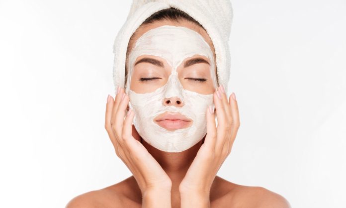 Beautiful woman with eyes closed and white clay facial mask on face isolated on white background